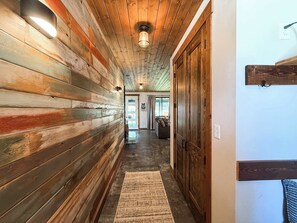A hallway with wooden walls, a rug, and a door with a hook. - New | 5 Min to Glacier | Hot Tub & Fire Pit (Martin City)