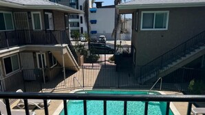 A swimming pool with a decorative metal fence, surrounded by buildings and palm trees. - Modern 1-bedroom apartment w/Pool in Popular Northpark Neighborhood (San Diego)