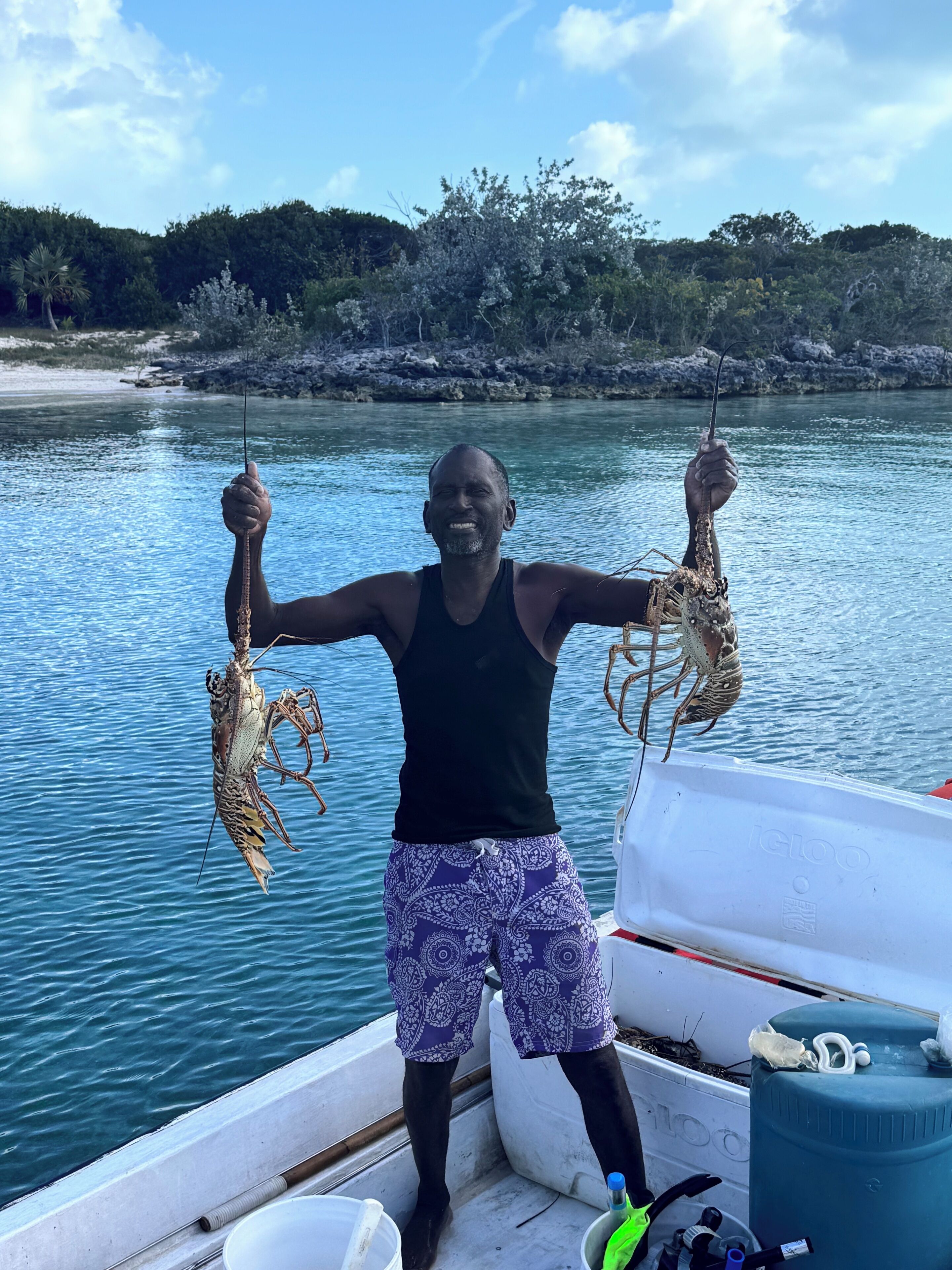 A person holding two lobsters on a boat with a calm water body and a forested shoreline in the background.