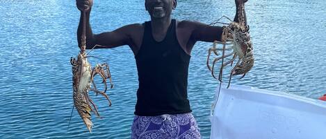 A person holding two lobsters on a boat with a calm water body and a forested shoreline in the background.