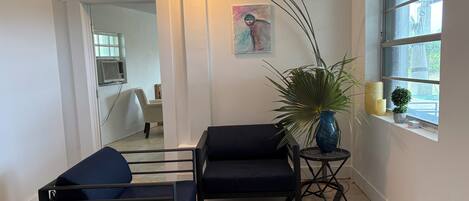 A room with two dark-colored sofas, a potted plant, a painting, and a window with a view.