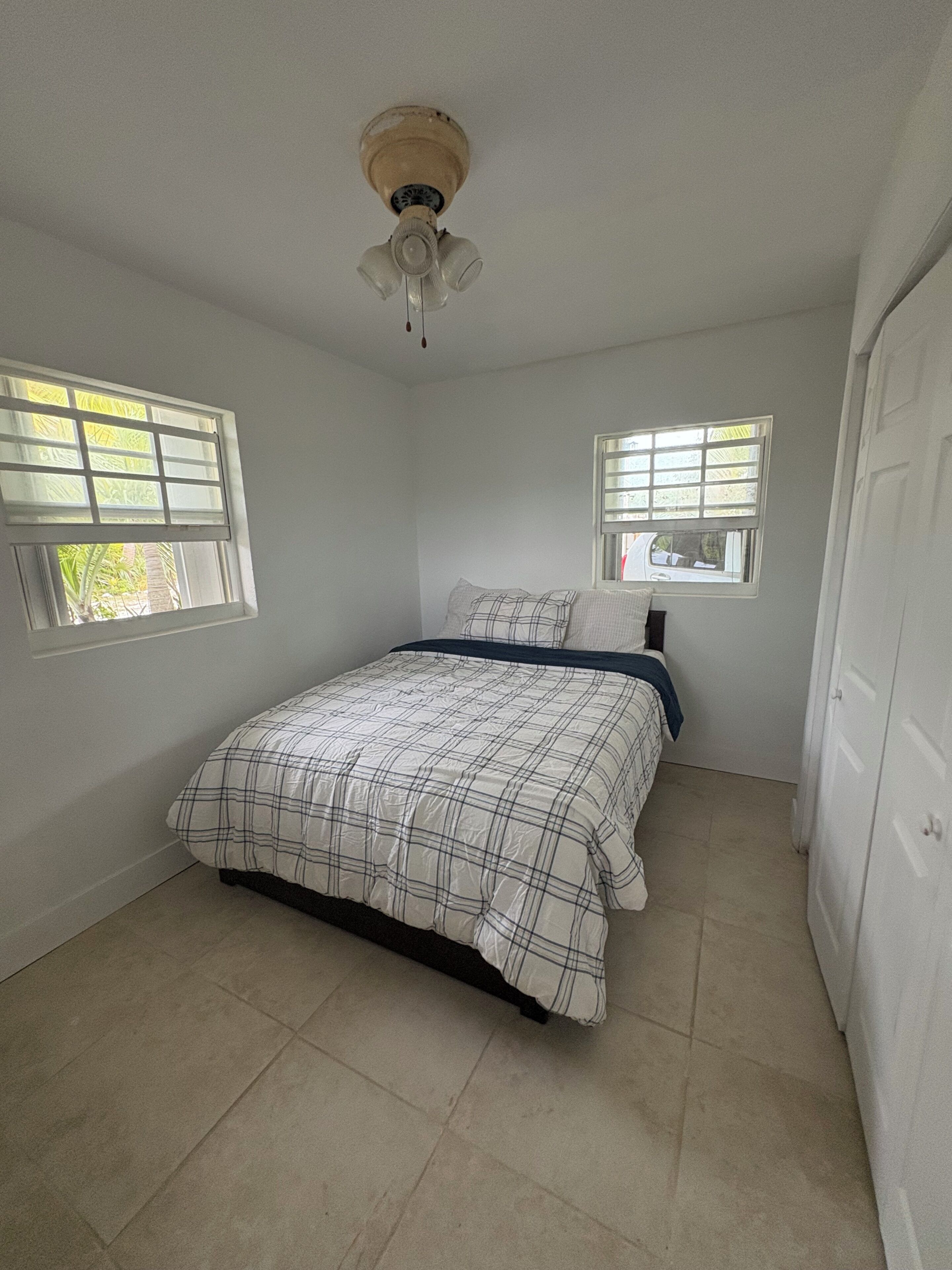 A bedroom with a bed, two windows, a ceiling fan, and a door.