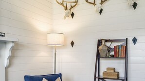 A blue armchair with a cushion, a lamp, a bookshelf with books, decorative antlers, and a patterned rug. - Panoramic Mountain Views + Private Hot Tub — Your Ultimate Shenandoah Valley Escape (Raphine)