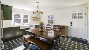 A kitchen with dark green cabinets, a wooden dining table with chairs, a chandelier, and a window with a view. - Panoramic Mountain Views + Private Hot Tub — Your Ultimate Shenandoah Valley Escape (Raphine)