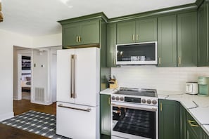 A kitchen with green cabinets, a white refrigerator, a stove, and a microwave.