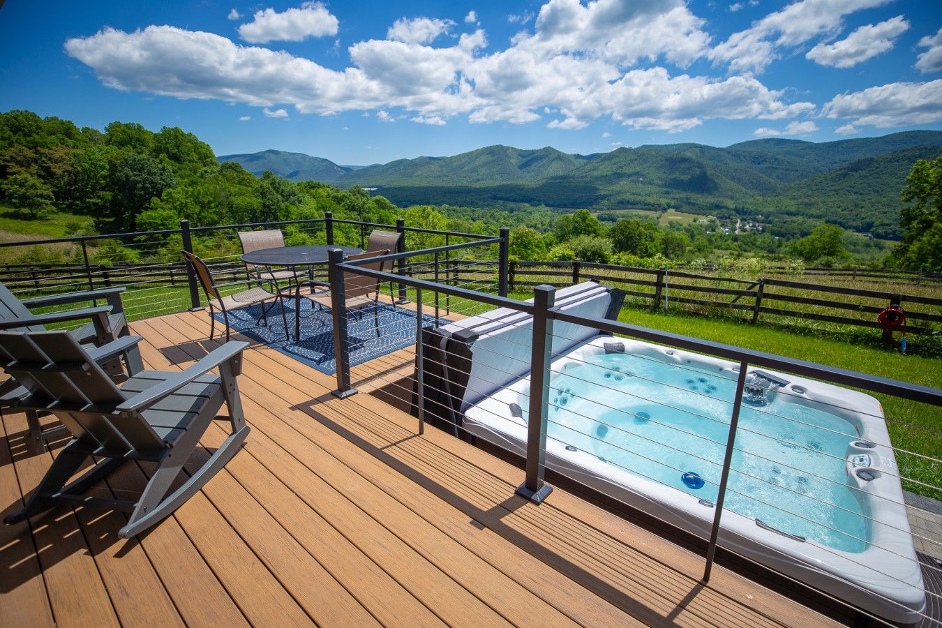 Ein Whirlpool auf einer Holzterrasse mit Blick auf grüne Hügel und Berge.