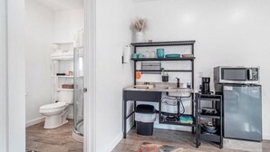 Cocina compacta con refrigerador, microondas y estantes con utensilios de cocina.