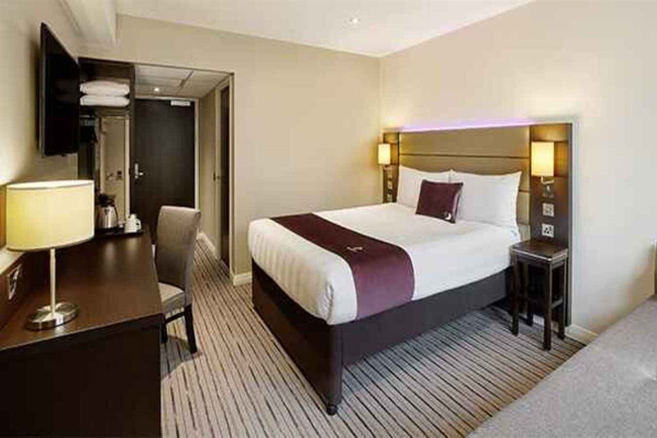 A hotel room with a bed, bedside tables, a desk, a chair, a TV, and a door.