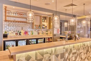 A bar area with a counter, shelves with bottles, and hanging light fixtures. - Premier Inn Plymouth City Centre (Plymouth)