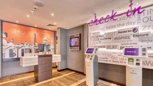Een hotel receptie met een incheckbalie, een digitaal kiosk en een muur met inspirerende uitspraken.