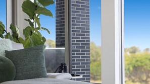 Ein Zimmer mit großem Fenster, einer Pflanze, einem Teleskop und einer Ziegelwand.