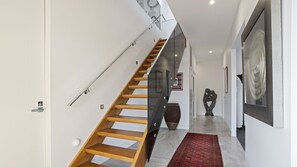 A modern staircase with wooden steps and glass railings, leading to a landing with a red patterned rug. - The Coral Esplanade with Pool (Mornington)