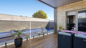 A covered outdoor area with a pool, wooden deck, and a table with chairs. - The Coral Esplanade with Pool (Mornington)