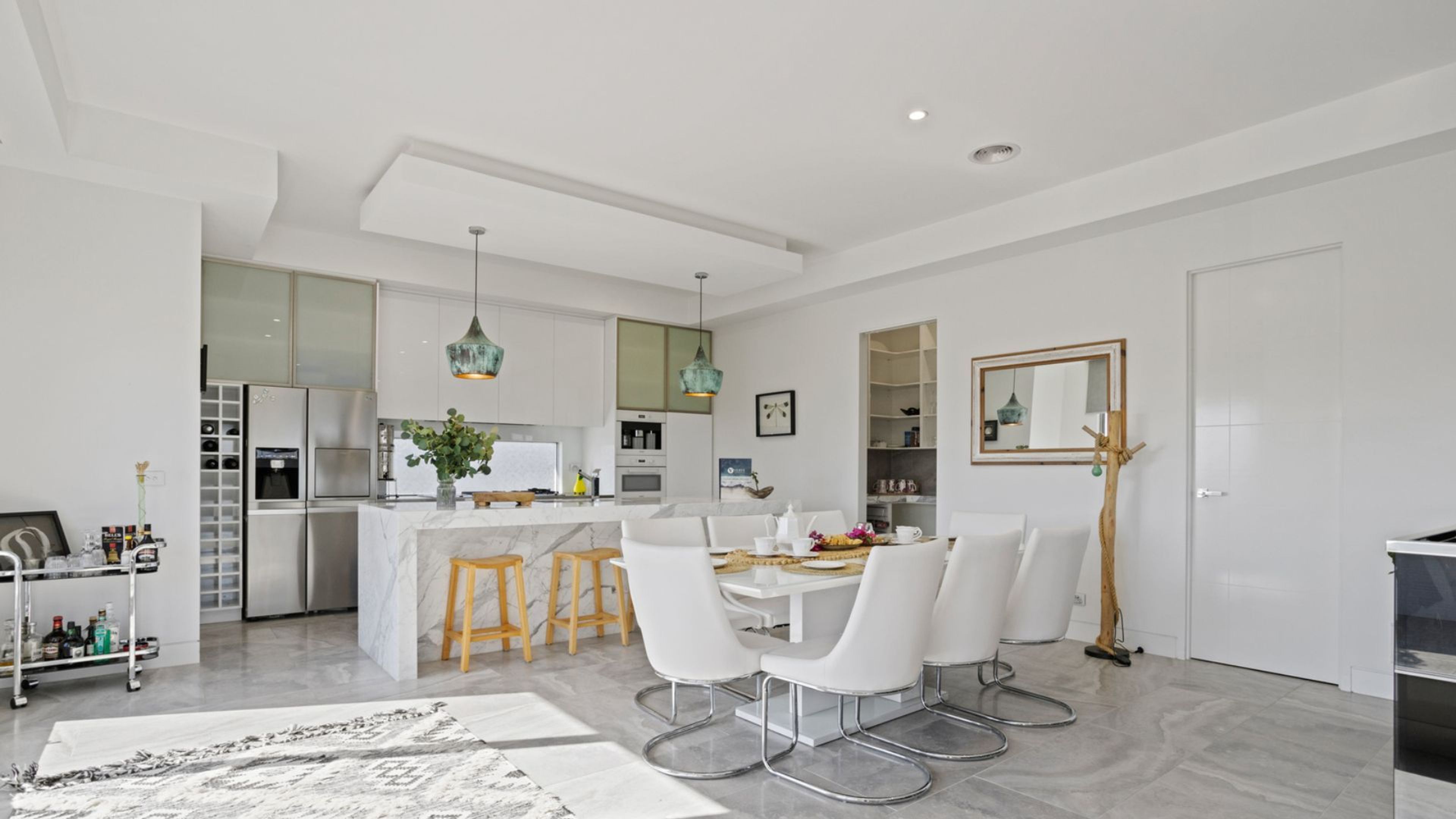 A modern kitchen with white cabinetry, a marble island, and pendant lighting.