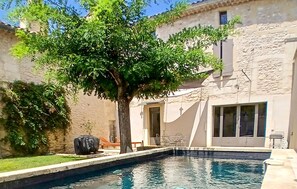 Una piscina con un árbol en el centro, un muro de piedra y un edificio con una puerta y ventanas.