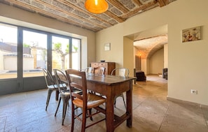 Un comedor con una mesa y sillas de madera, ventanas amplias y techo de piedra.