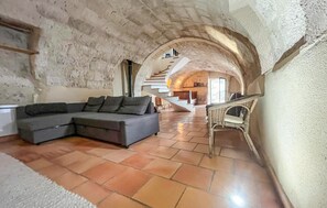 Un interior con pared de piedra, un sofá seccional gris, una silla de mimbre y una escalera que sube a un nivel superior.