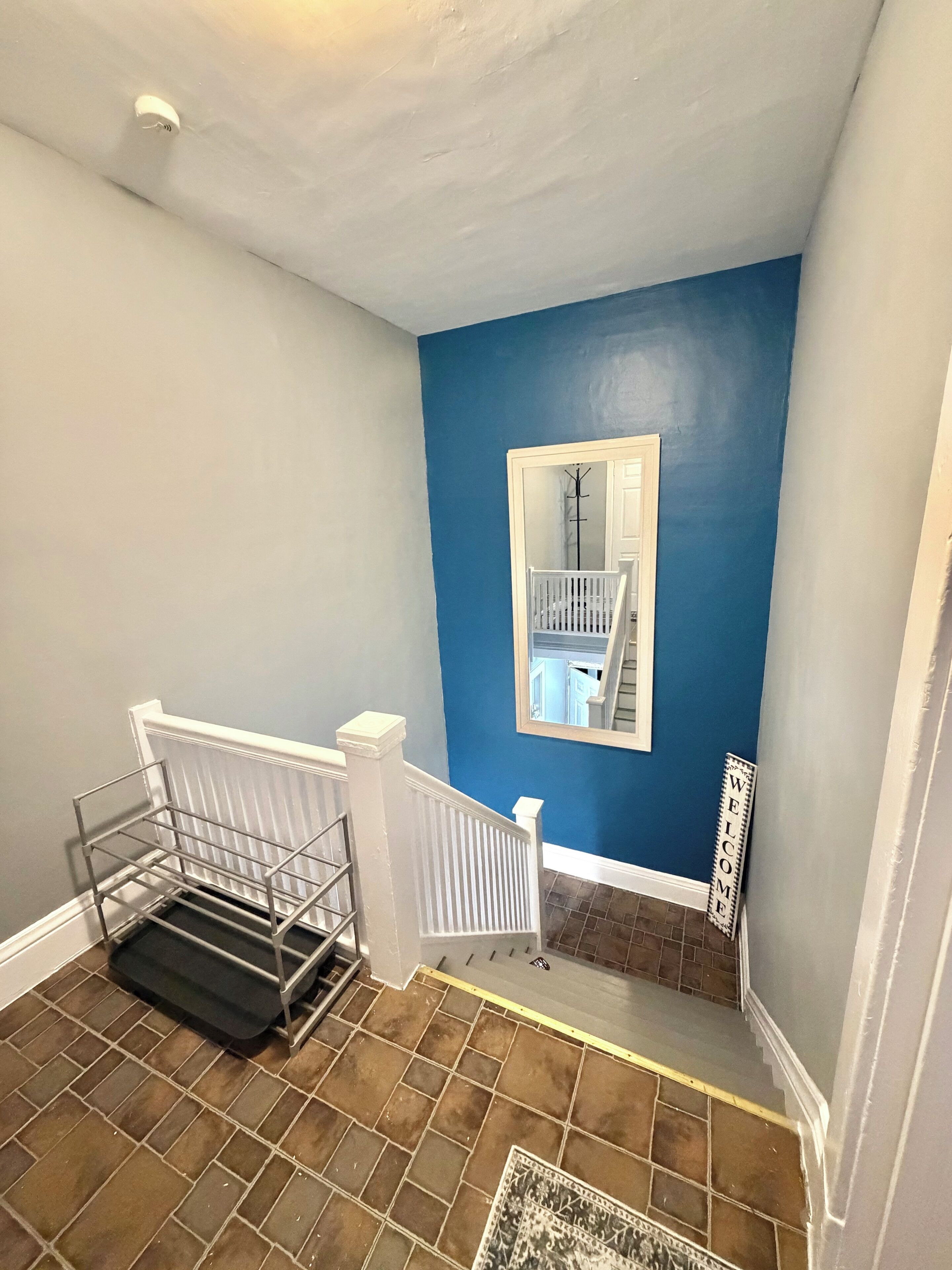 Un escalier avec une rampe blanche, un mur bleu, une porte blanche et une pancarte de bienvenue.