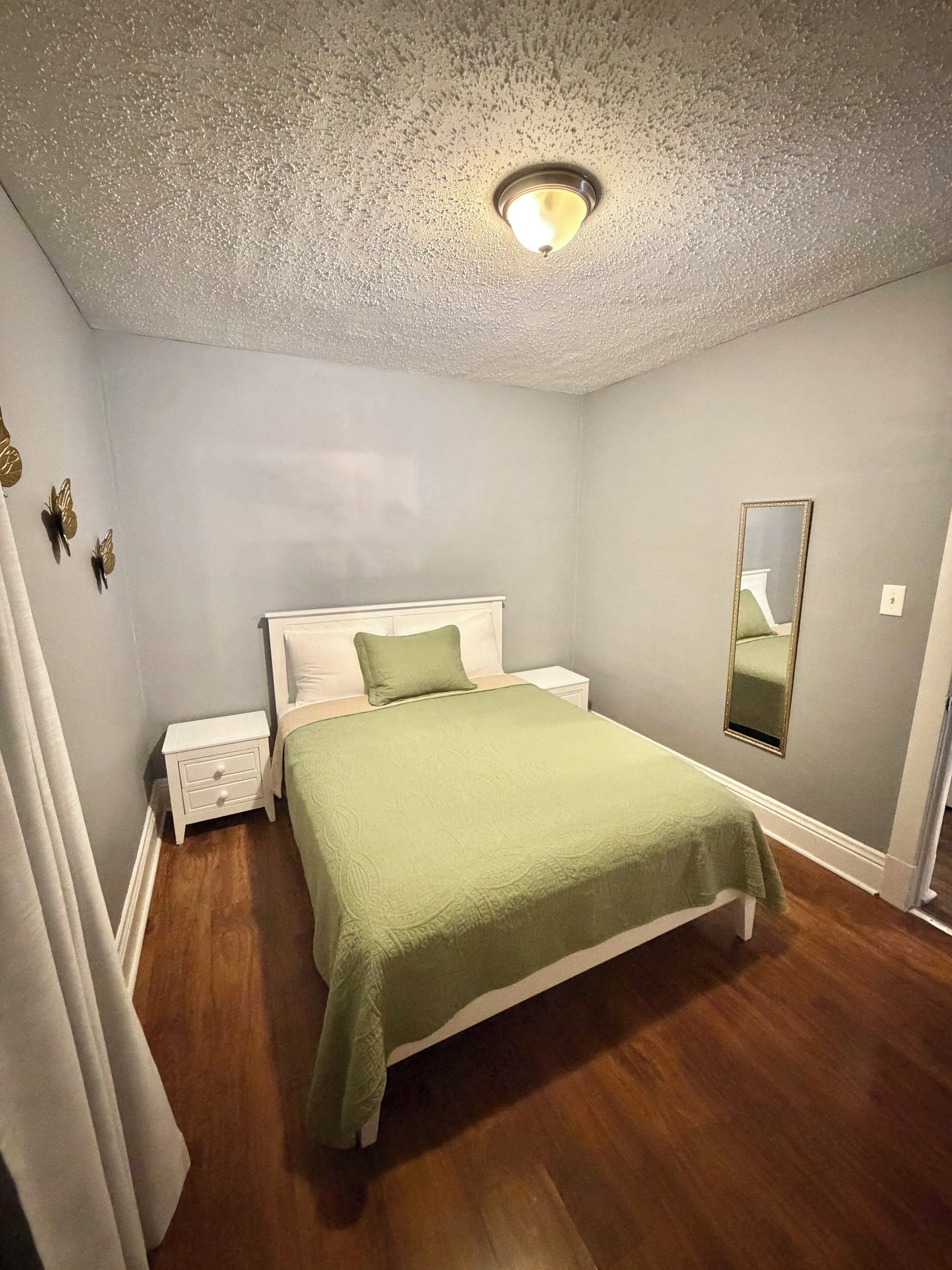 Een slaapkamer met een bed, nachtkastjes, een spiegel en een plafondlamp.