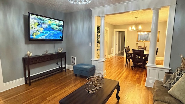 A living room with a dark wooden coffee table, a television on the wall, and a dining area with a chandelier.