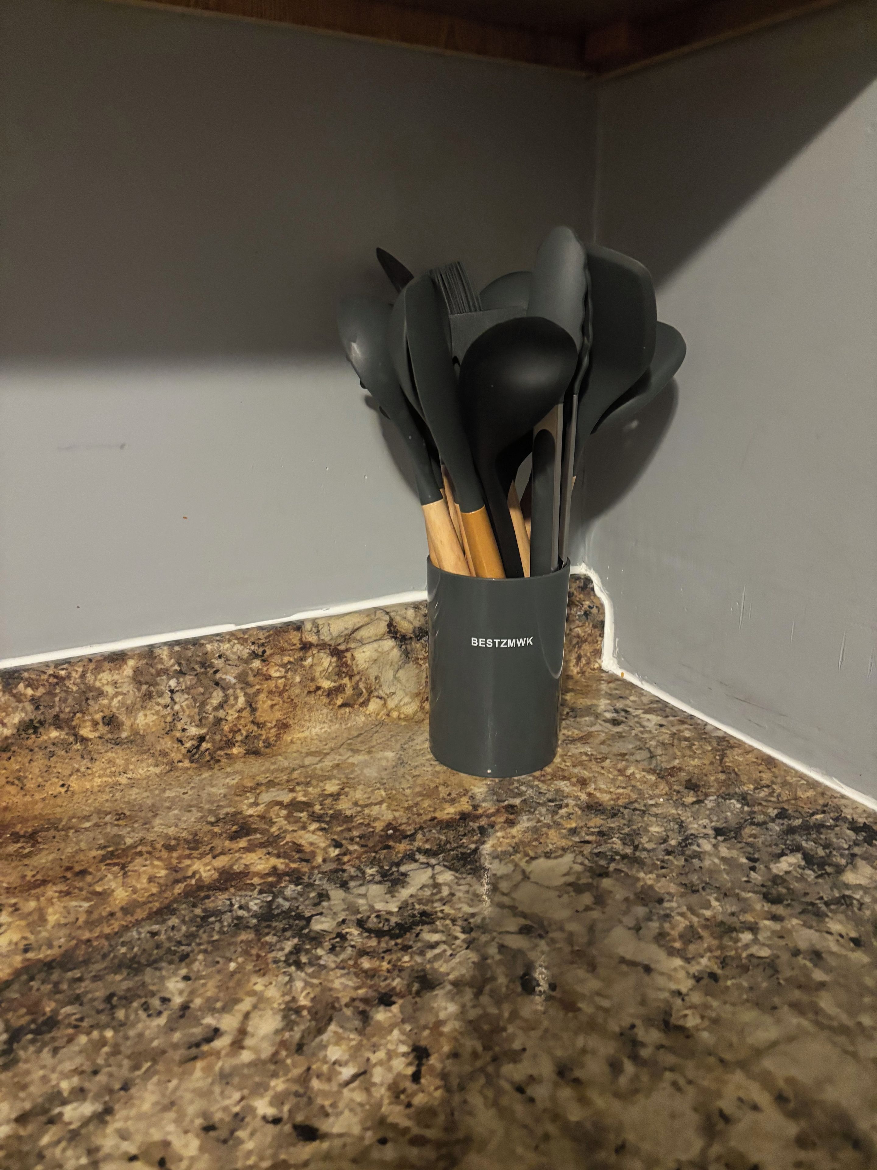 En holder til køkkenredskaber med en etiket på en granitbordplade.
