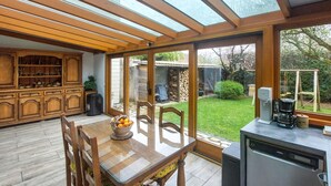 Eine Küche mit Esstisch, Stühlen, einer Kaffeemaschine und Blick auf den Garten durch große Fenster.