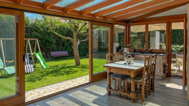 Ein sonnendurchfluteter Raum mit einem Holztisch und Stühlen, einer Schaukel und Blick auf einen Garten.