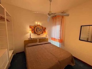 Quarto com cama, ventoinha no teto, espelho fixado na parede e um quadro.
