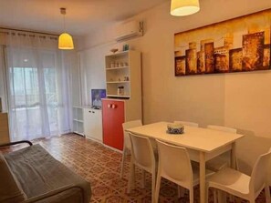 A dining area with a table and chairs, a red cabinet, and a painting on the wall. - Holiday apartment mit Klimaanlage und Balkon (Lido di Jesolo)