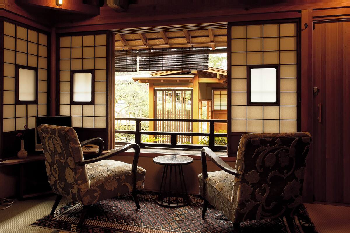 A traditional Japanese room with tatami flooring, a low table, and two chairs.