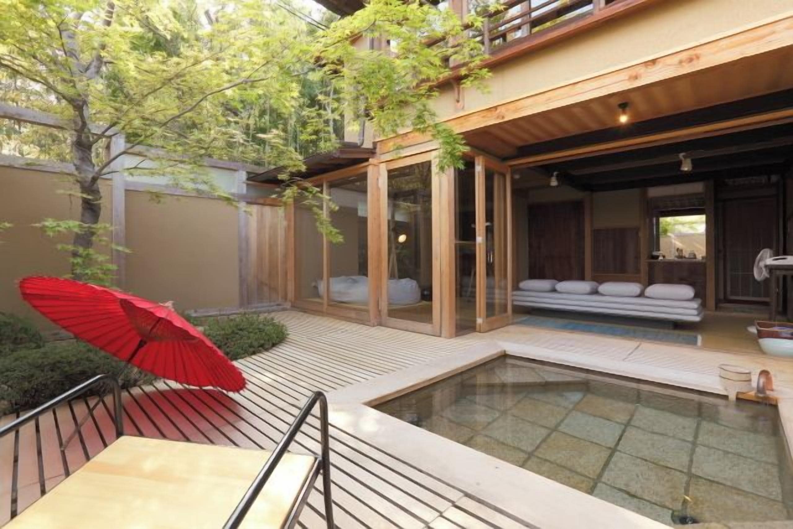 A modern outdoor pool area with a glass enclosure, a red umbrella, and a seating area with cushions.