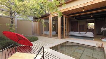 A modern outdoor pool area with a glass enclosure, a red umbrella, and a seating area with cushions.