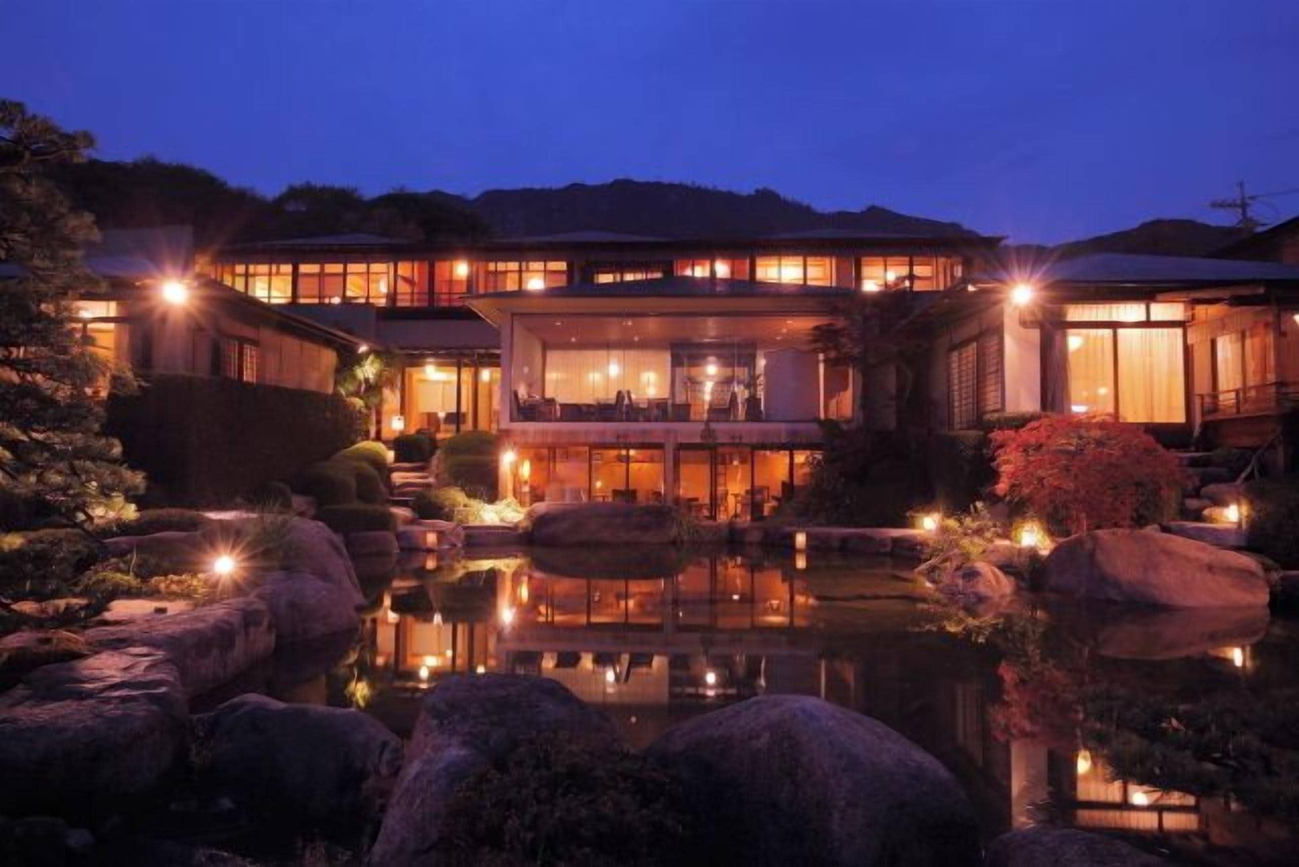 A traditional Japanese-style building with a reflective pond, large rocks, and well-lit exterior.