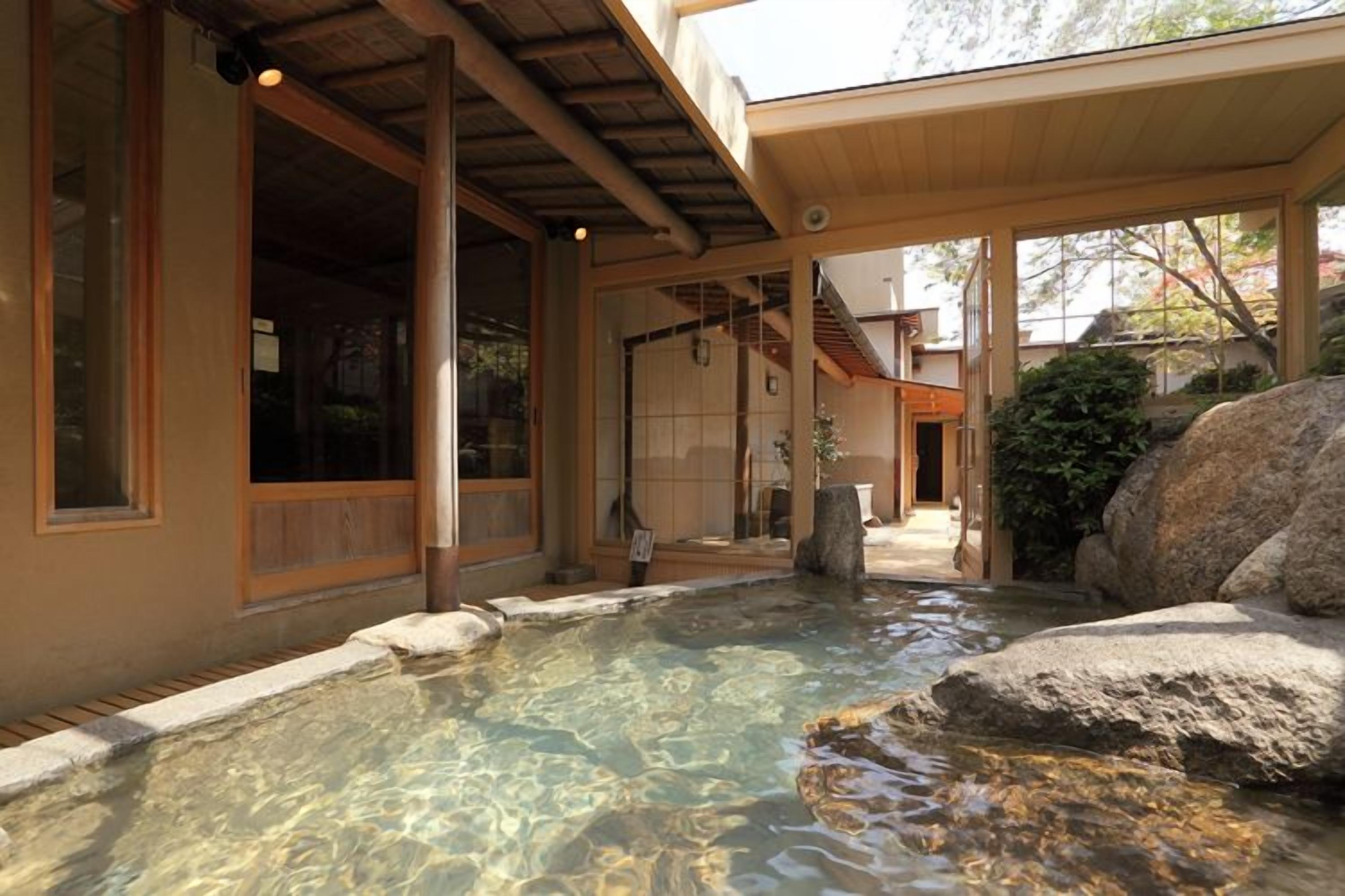 A traditional Japanese building with a clear outdoor pool, wooden beams, and a stone structure.