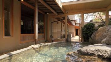 A traditional Japanese building with a clear outdoor pool, wooden beams, and a stone structure.