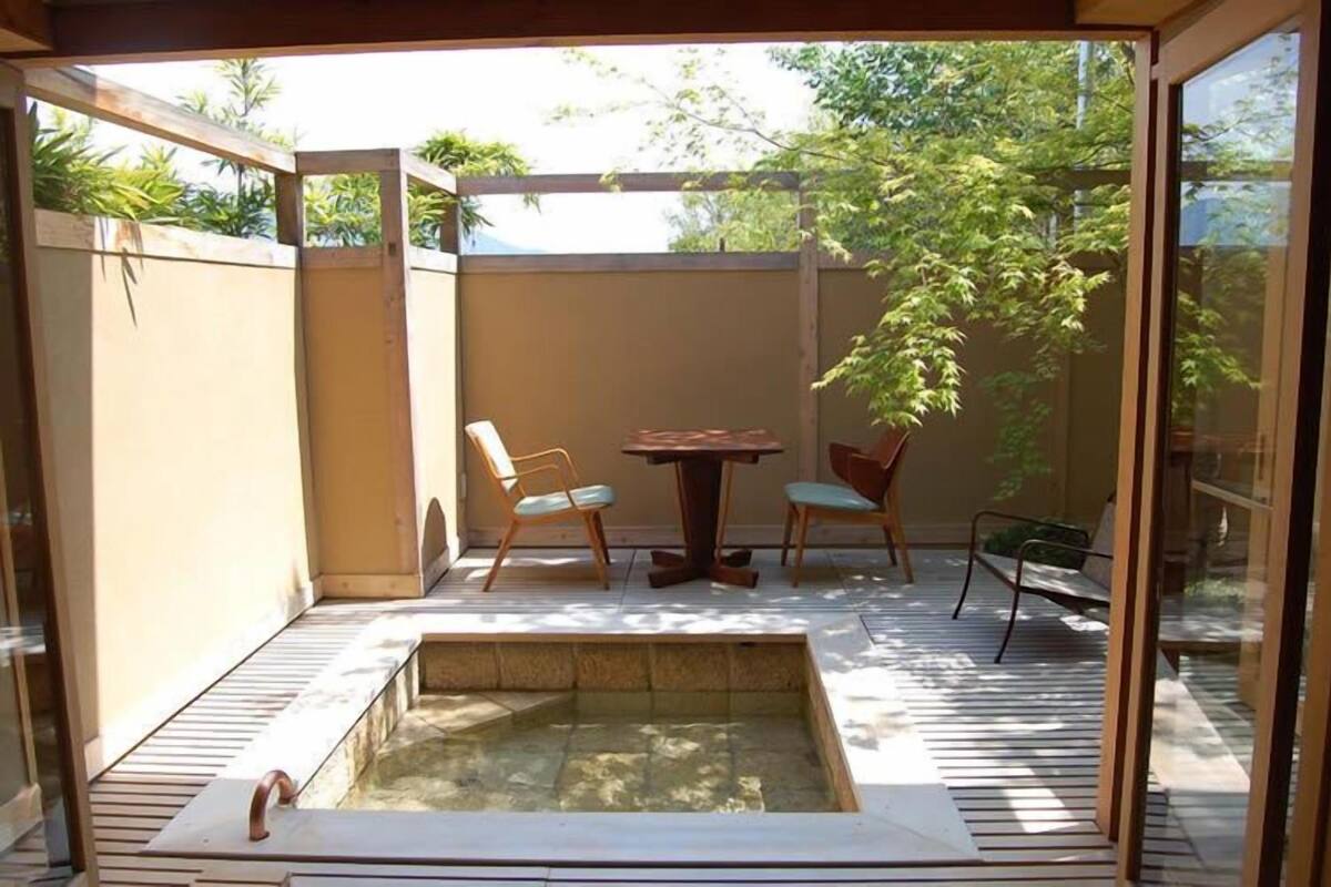 A sunlit patio with a hot tub, two wooden tables, and chairs.