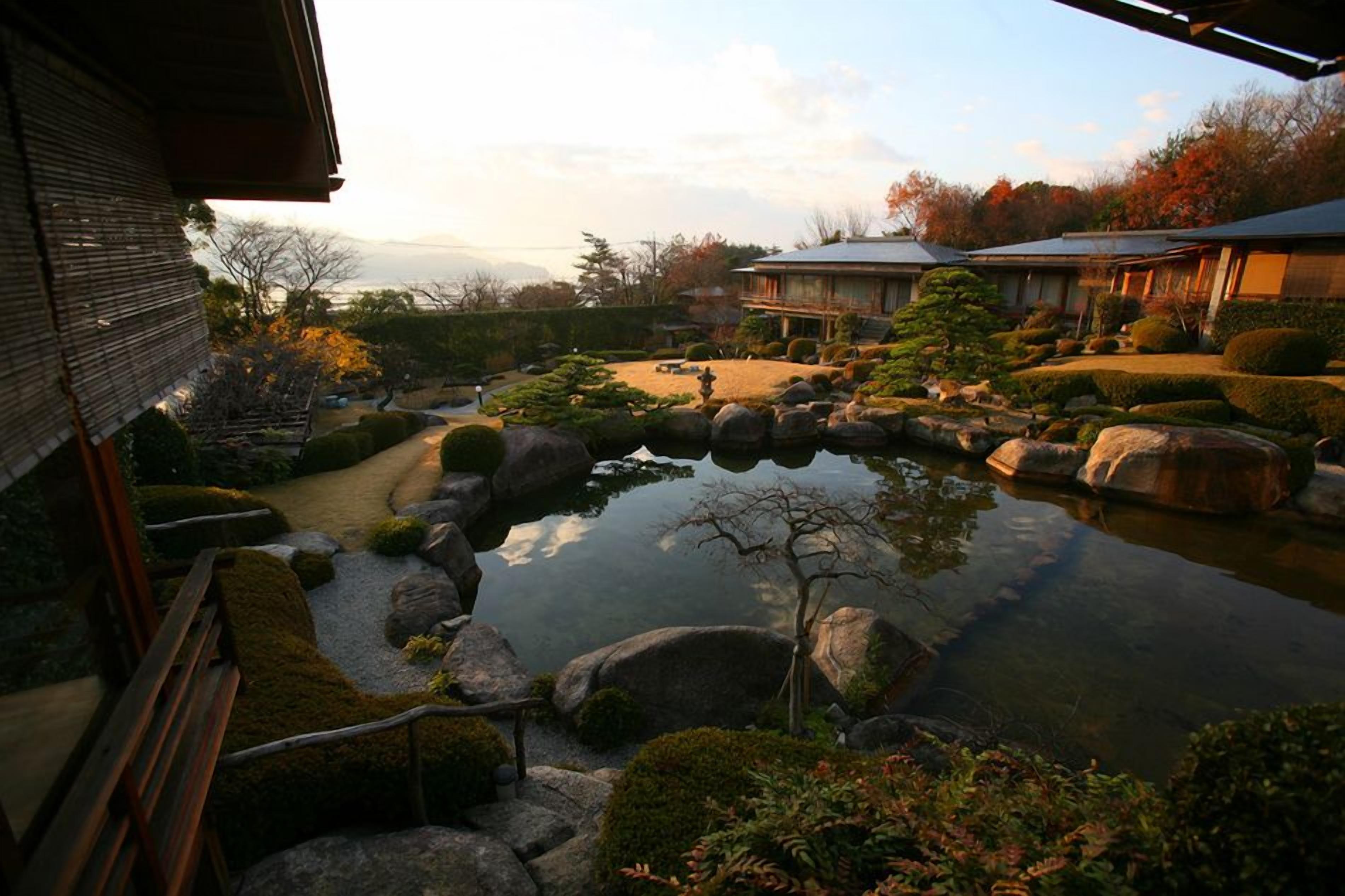 A traditional Japanese garden with a pond, rocks, and a wooden building.