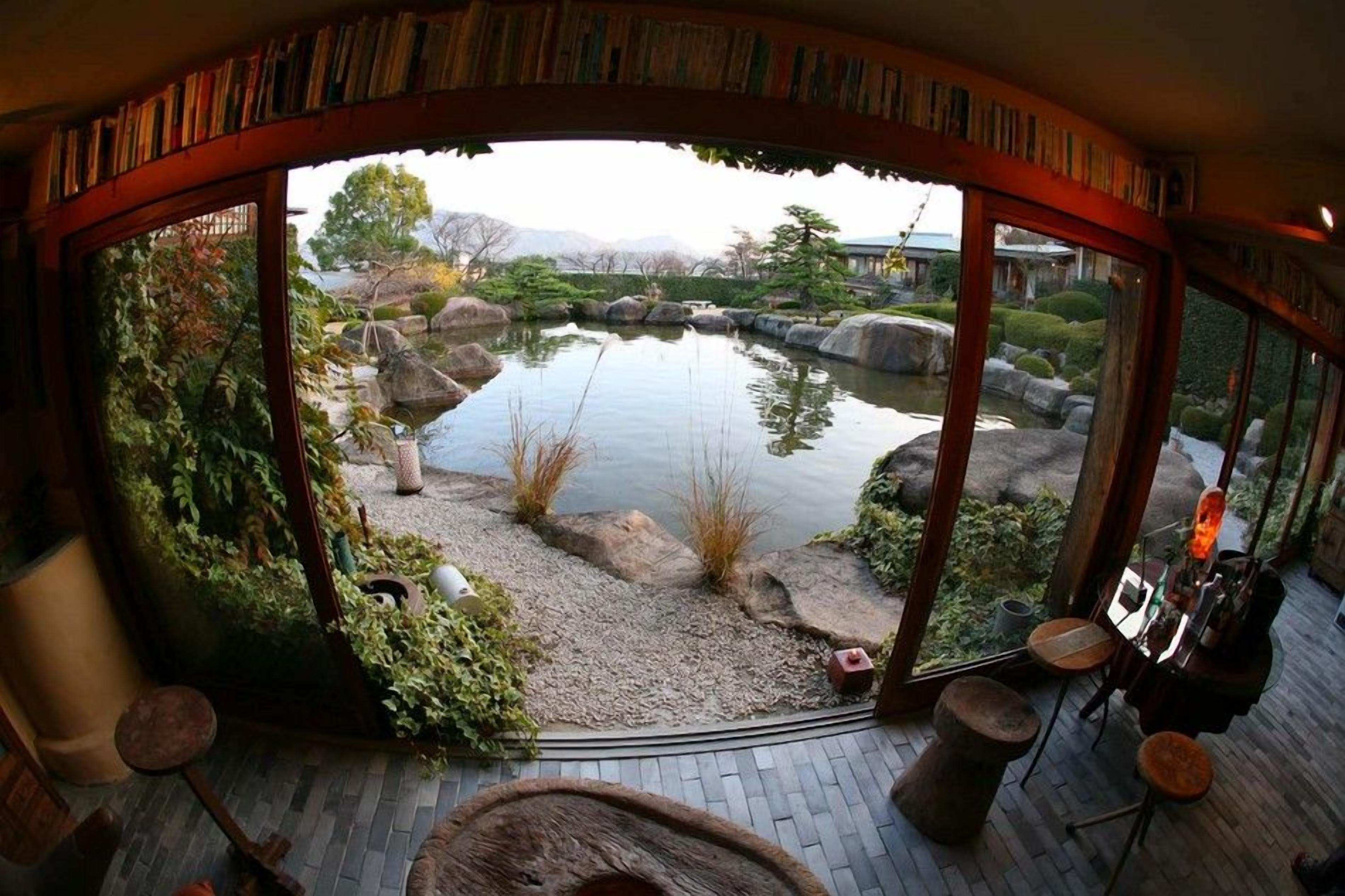 A circular room with a view of a pond, surrounded by rocks and plants, and furnished with a table and chairs.