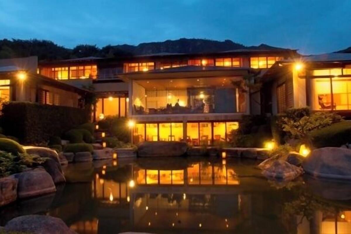 A multi-story building with a reflective pool in front, surrounded by rocks and plants.
