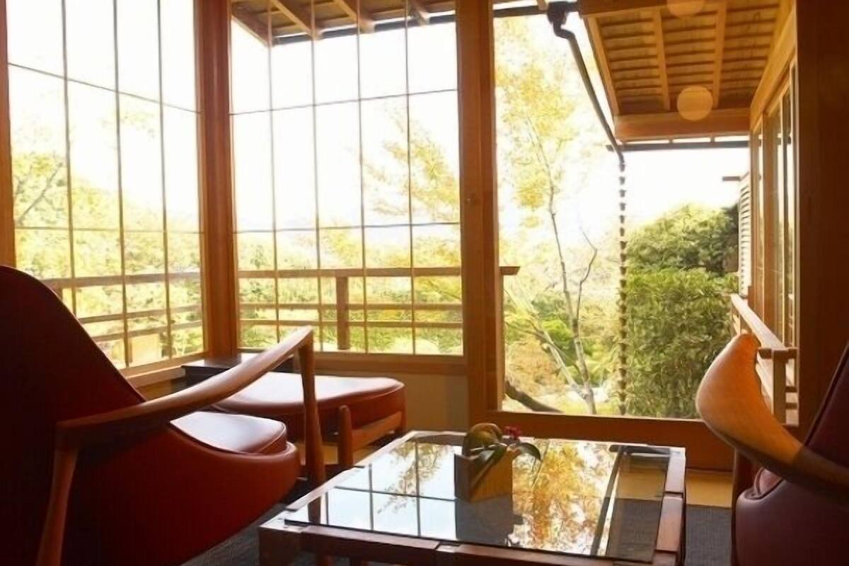 A room with a view through large windows, a glass-top table, and a red chair.