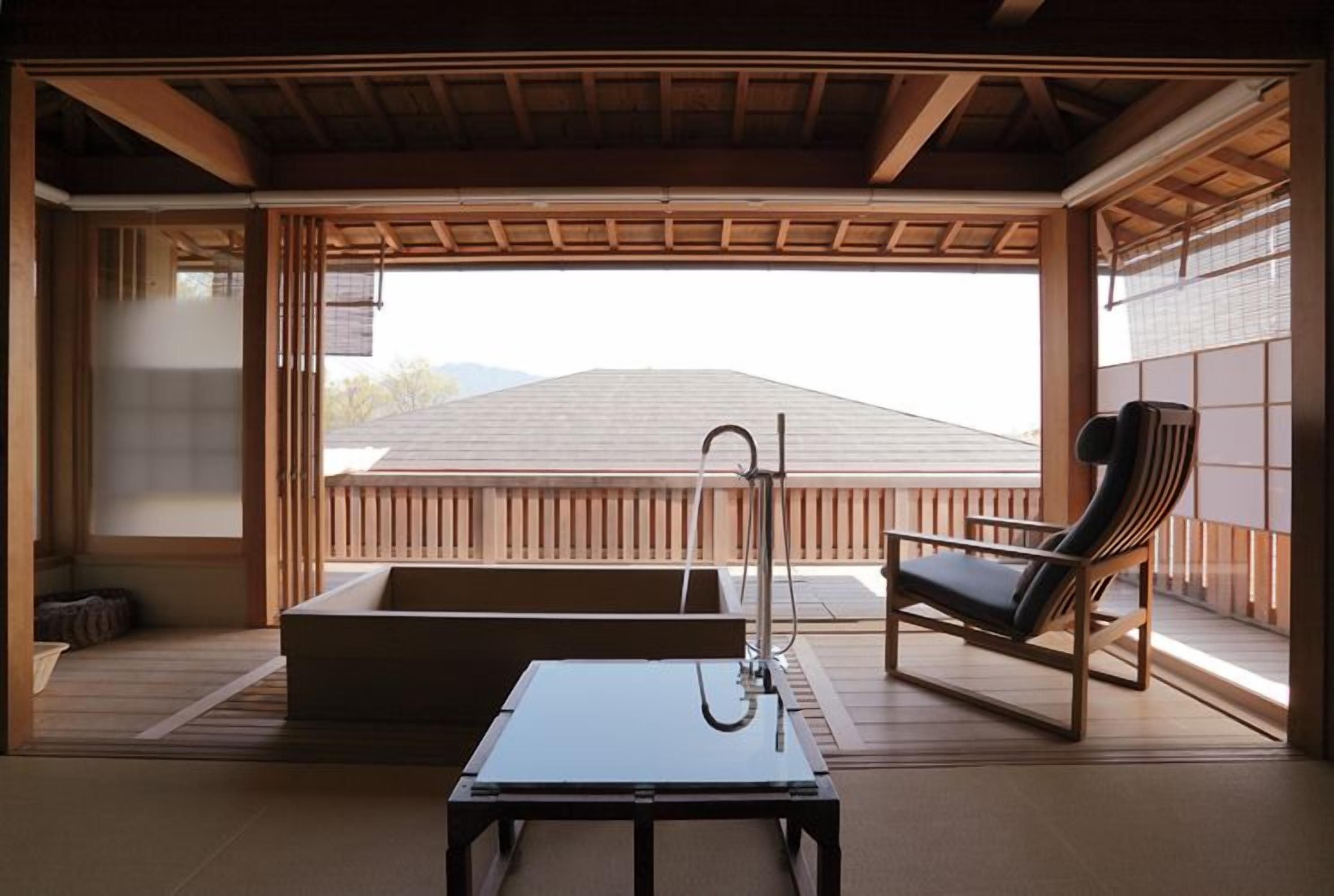 A traditional Japanese room with tatami flooring, a low table, a cushioned bench, and a view of a mountain.