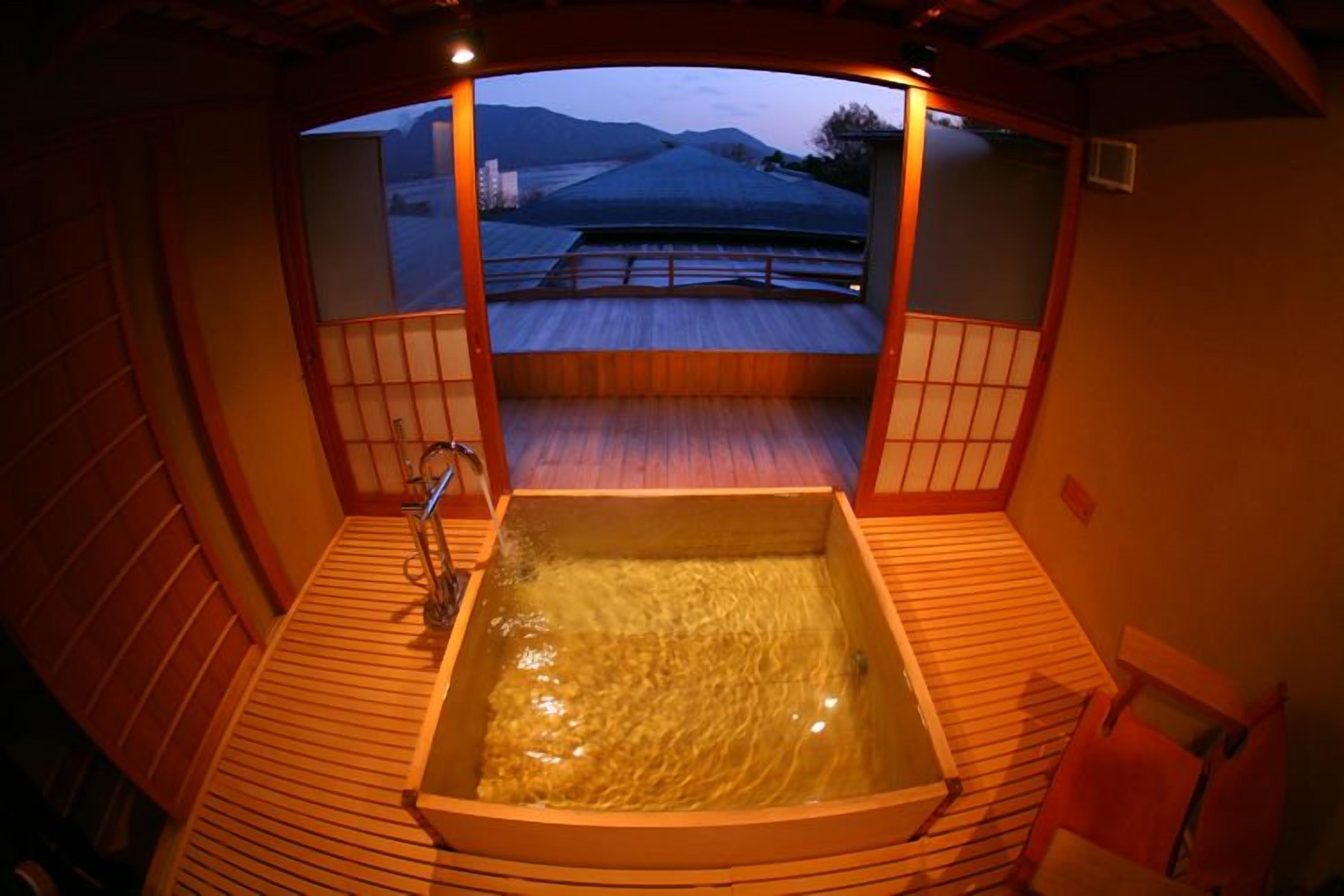A traditional Japanese onsen with a wooden deck and a view of the landscape.