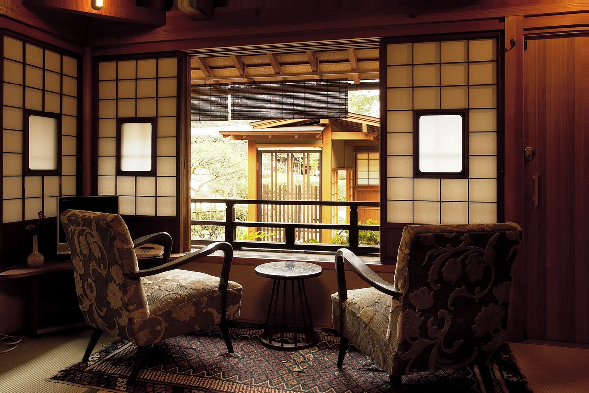 A traditional Japanese room with tatami flooring, a low table, and two chairs.