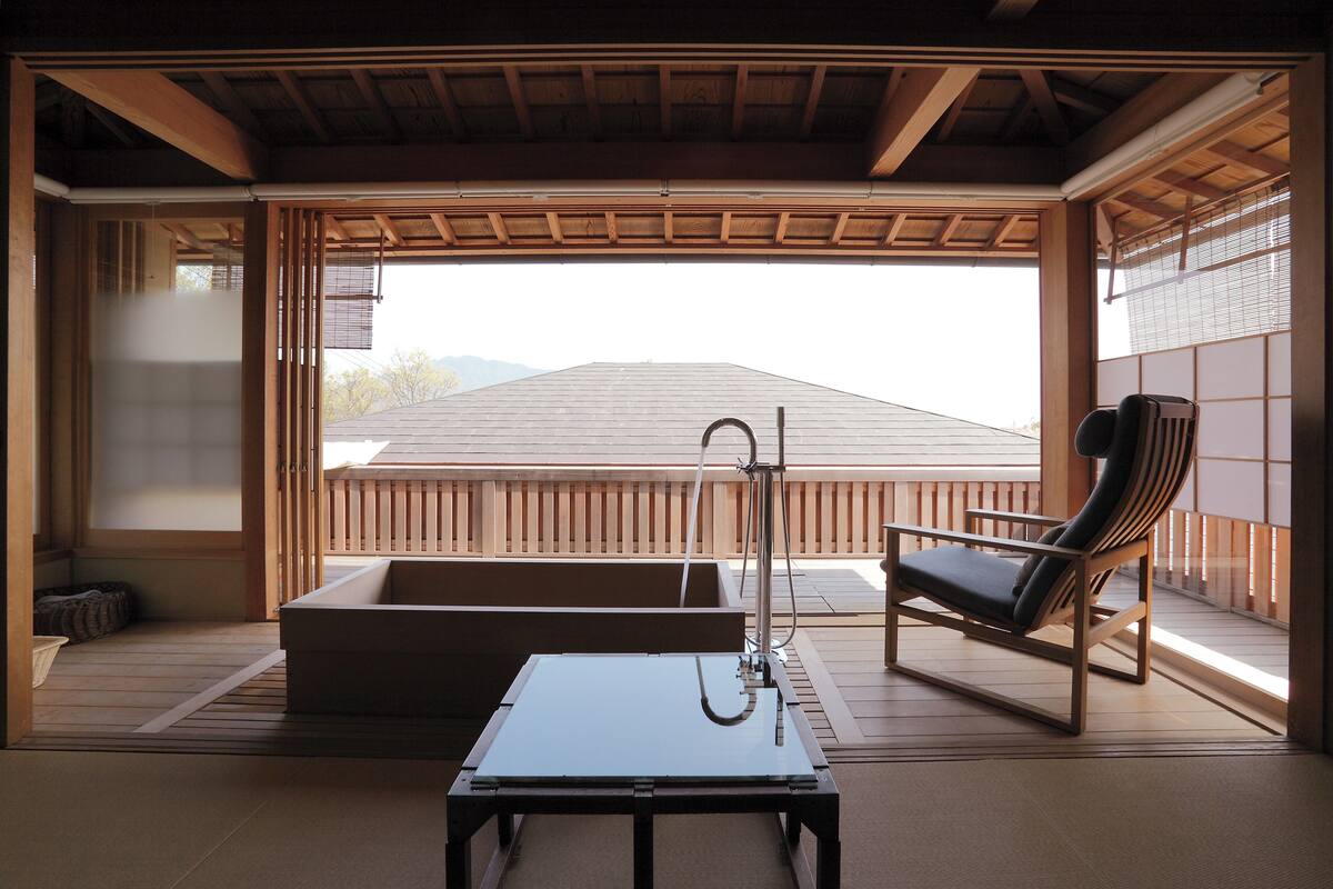 A traditional Japanese room with tatami flooring, a tatami mat table, a black cushioned chair, and a wooden ceiling.