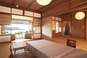 A traditional Japanese room with tatami flooring, a low table, and a bed with a white bedspread. - Miyahama Onsen Teien no Yado Sekitei (Hatsukaichi)