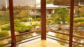 A traditional Japanese room with tatami flooring, a wooden table, and a view of a garden through large windows.
