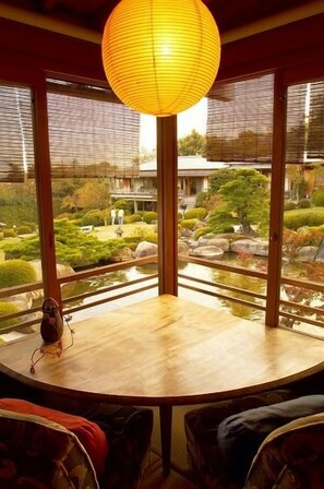 A traditional Japanese room with tatami flooring, a wooden table, and a view of a garden through large windows. - Miyahama Onsen Teien no Yado Sekitei (Hatsukaichi)