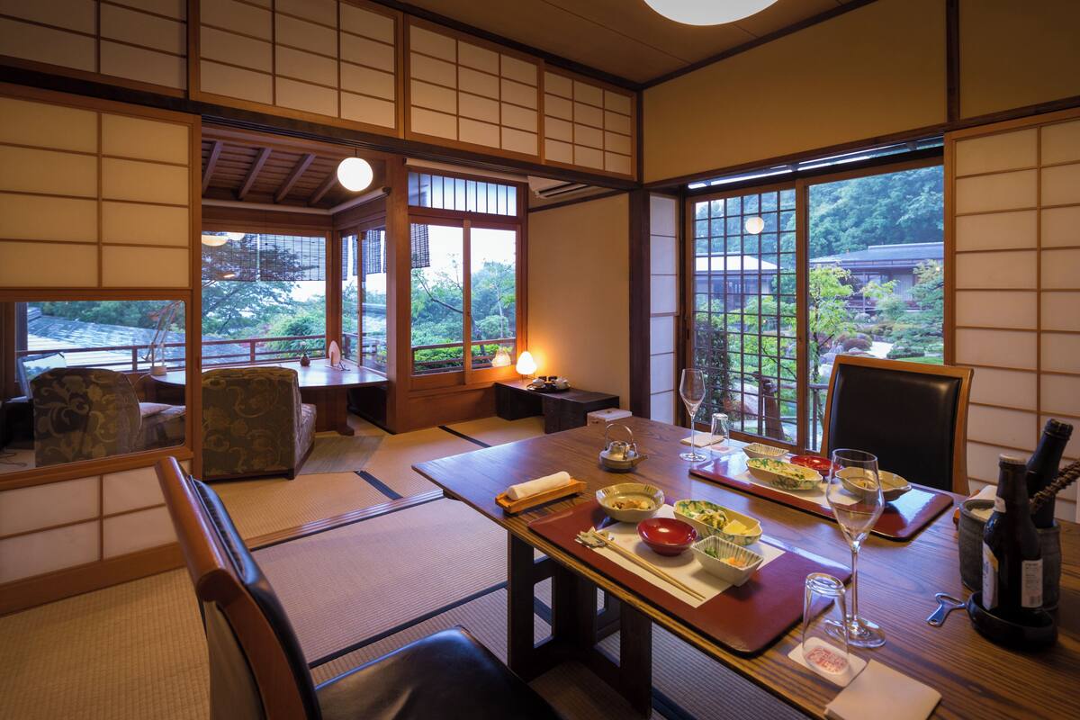 A traditional Japanese room with tatami flooring, a low table set for dining, and a view of a garden.