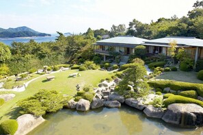 A traditional Japanese-style building with a garden, including a pond and rock formations. - Miyahama Onsen Teien no Yado Sekitei (Hatsukaichi)