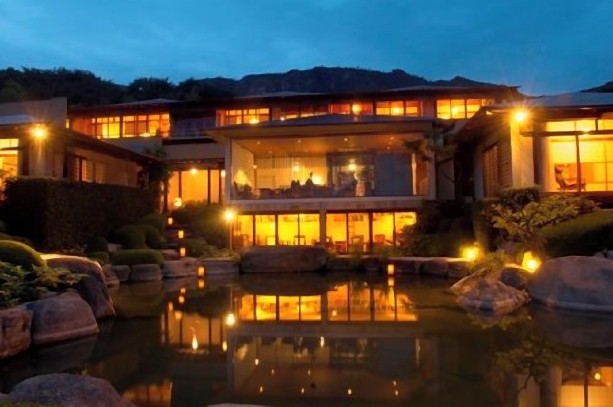 A multi-story building with a reflective pool in front, surrounded by rocks and plants.